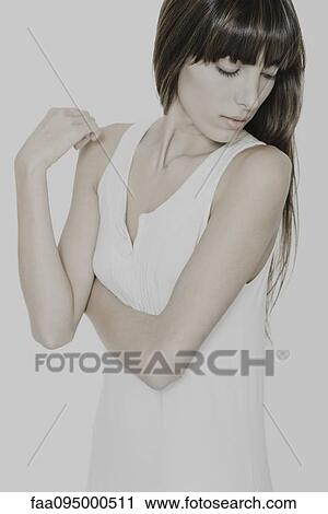 Stock Image - Young woman in dress, arms folded, looking down. Fotosearch