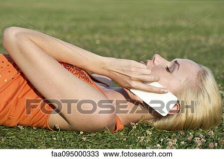 Stock Image - Young woman lying on grass talking on smartphone. Fotosearch