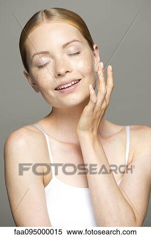 Stock Photography - Young woman moisturizing face, eyes closed. Fotosearch