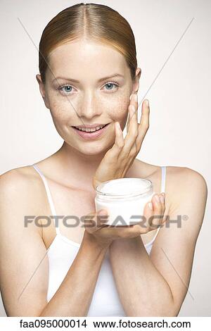 Picture - Young woman moisturizing face. Fotosearch