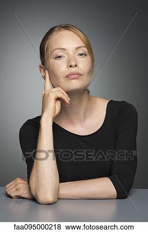 Stock Photo - Young woman sitting with hand under chin, portrait. Fotosearch