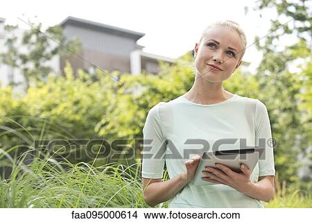 Picture - Young woman using digital tablet outdoors. Fotosearch