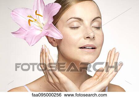 Stock Photograph - Young woman wearing lily in hair, eyes closed, portrait. Fotosearch