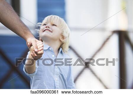 Stock Image - Boy holding father's hand, looking up at father. Fotosearch