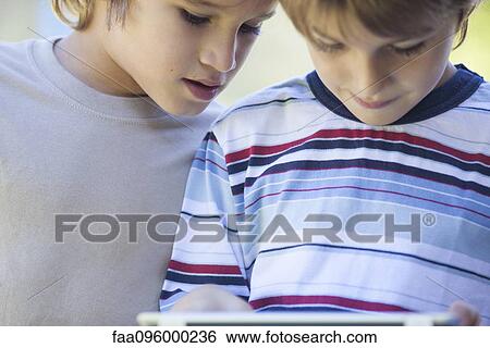 Boys looking down at digital tablet View Large Photo Image Stock Photograph - Boys looking down at digital tablet. Fotosearch