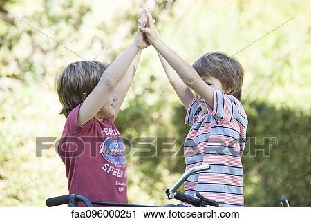 Stock Image - Boys on bicycles giving high fives. Fotosearch