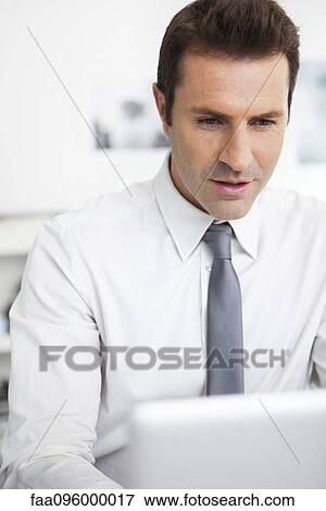 Stock Photo - Businessman using laptop working in office. Fotosearch