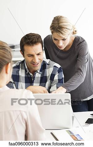 Colleagues gathered around laptop collaborating on work project View Large Photo Image Stock Image - Colleagues gathered around laptop collaborating on work project. Fotosearch