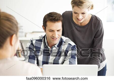 Stock Photograph - Colleagues gathered around laptop computer collaborating on work project. Fotosearch
