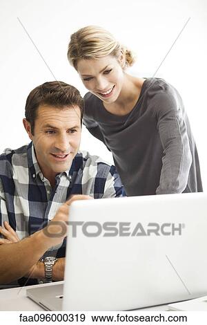 Stock Photo - Colleagues looking at laptop computer together. Fotosearch