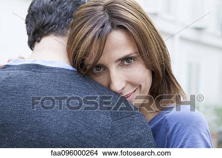 Picture - Couple embracing, woman looking at camera. Fotosearch