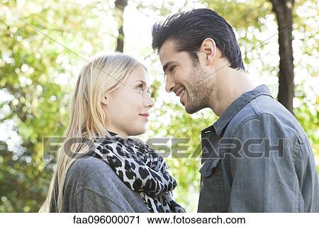 Couple standing together outdoors, looking into each other's eyes View Large Photo Image Stock Image - Couple standing together outdoors, looking into each other's eyes. Fotosearch