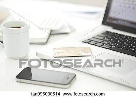 Picture - Credit card resting on laptop computer, smartphone and cup of coffee nearby. Fotosearch