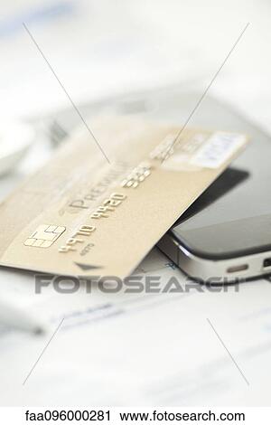 Stock Image - Credit card resting on smartphone. Fotosearch