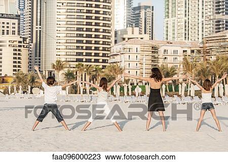 Stock Image - Family standing in a row on beach, holding hands, rear view. Fotosearch