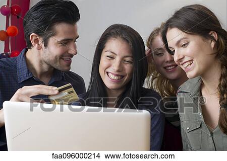 Picture - Friends gathered around laptop computer preparing to use credit card for online purchase. Fotosearch