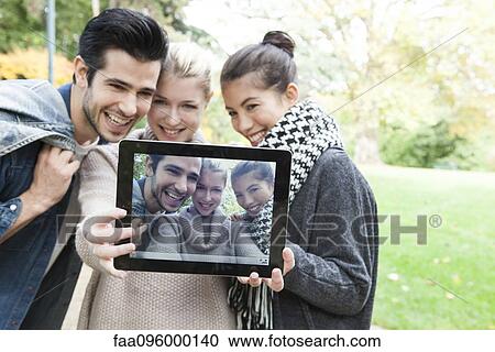 Stock Image - Friends photographing themselves with digital tablet outdoors. Fotosearch