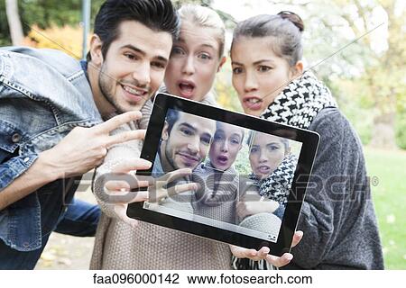 Stock Image - Friends photographing themselves with digital tablet outdoors. Fotosearch
