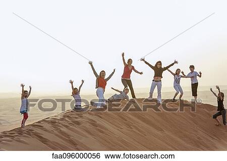 Stock Photograph - Group of people standing on top of desert dune with arms raised in air. Fotosearch