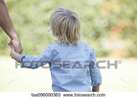 Stock Image - Little boy holding father's hand, rear view. Fotosearch