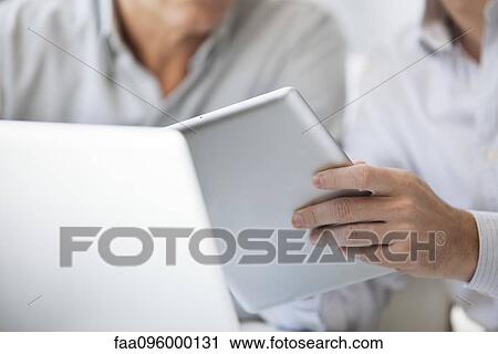 Stock Image - Men using digital tablet and laptop computer, cropped. Fotosearch