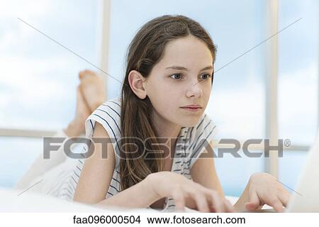 Picture - Preteen girl lying on stomach using laptop computer. Fotosearch