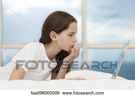 Preteen girl lying on stomach using laptop computer View Large Photo Image Stock Photograph - Preteen girl lying on stomach using laptop computer. Fotosearch