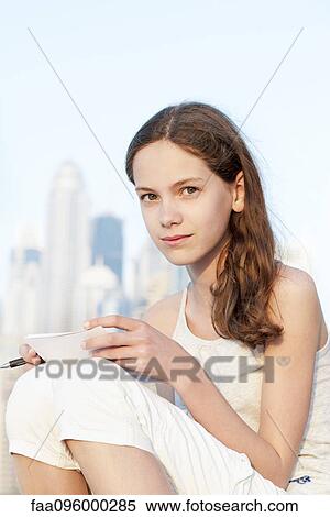 Preteen girl sitting outdoors, holding pen and paper View Large Photo Image Stock Photography - Preteen girl sitting outdoors, holding pen and paper. Fotosearch