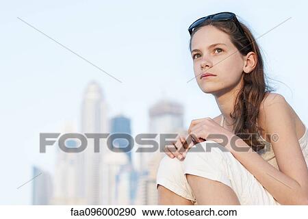 Stock Image - Preteen girl sitting outdoors, looking up in thought. Fotosearch