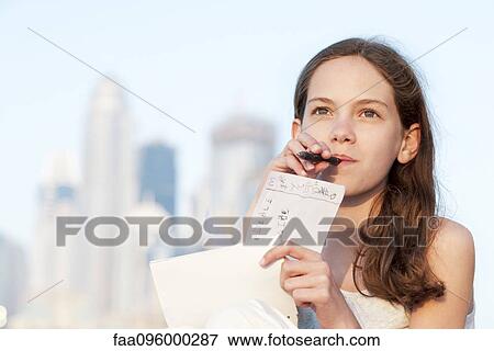 Preteen girl sitting outdoors with pen in mouth, looking up in thought View Large Photo Image Stock Photo - Preteen girl sitting outdoors with pen in mouth, looking up in thought. Fotosearch