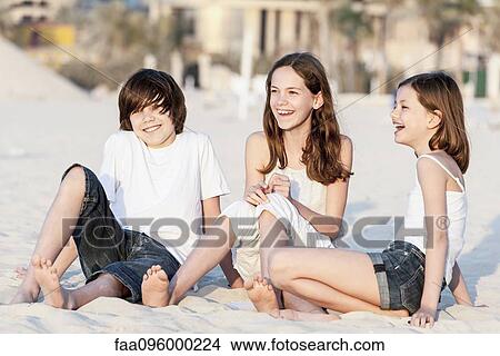 Siblings sitting together on sand at the beach View Large Photo Image Picture - Siblings sitting together on sand at the beach. Fotosearch