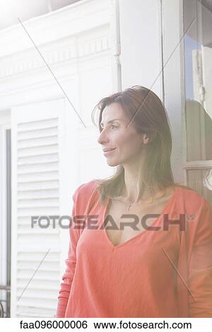Stock Photograph - Woman by open window looking at view. Fotosearch