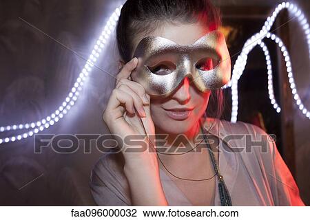 Stock Image - Woman holding party mask in front of face, portrait. Fotosearch