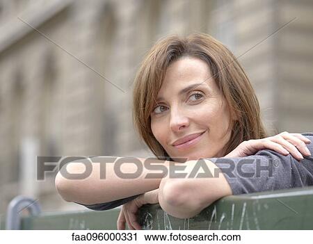 Stock Image - Woman leaning against railing, looking away in thought, portrait. Fotosearch