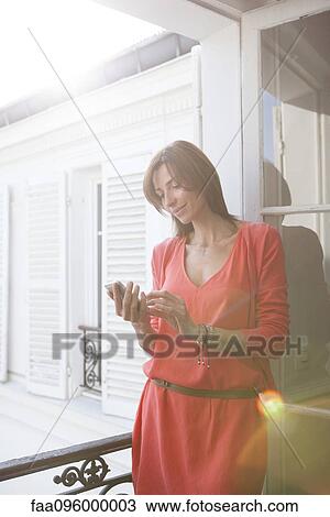 Stock Image - Woman on balcony using smartphone. Fotosearch