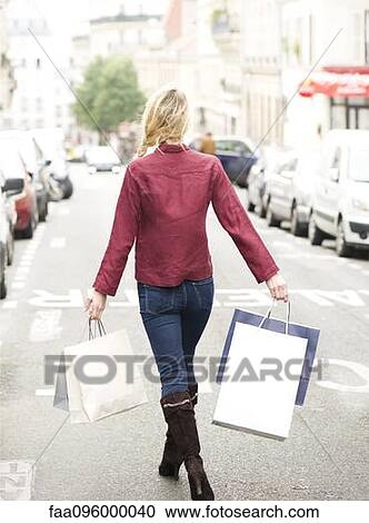 Stock Image - Woman walking in street with shopping bags, rear view. Fotosearch
