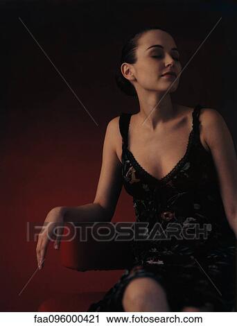 Stock Image - Woman wearing dress, sitting in chair, looking away. Fotosearch