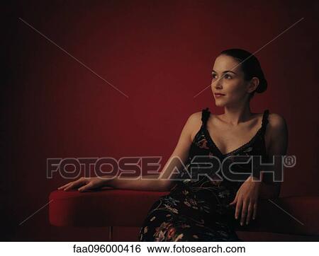 Stock Photograph - Woman wearing dress, sitting in chair, looking away. Fotosearch