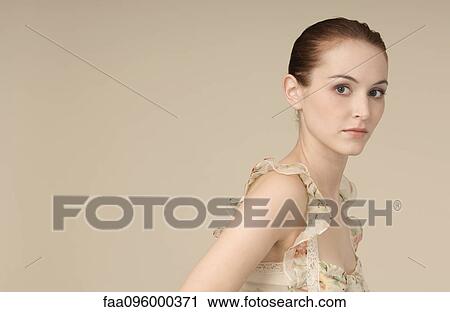 Stock Image - Woman wearing ruffly dress, hair in bun, looking at camera, portrait. Fotosearch