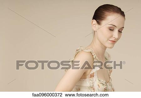 Stock Image - Woman wearing ruffly dress, hair in bun, eyes closed, portrait. Fotosearch