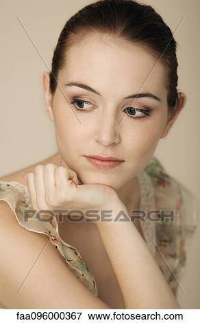 Stock Photo - Woman with hand under chin, wearing ruffly dress, hair in bun, portrait. Fotosearch