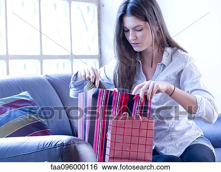 Stock Photograph - Young woman examining her purchases from recent shopping spree. Fotosearch