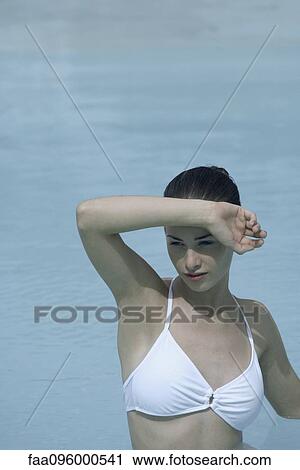 Stock Image - Young woman in swimming pool shielding eyes. Fotosearch