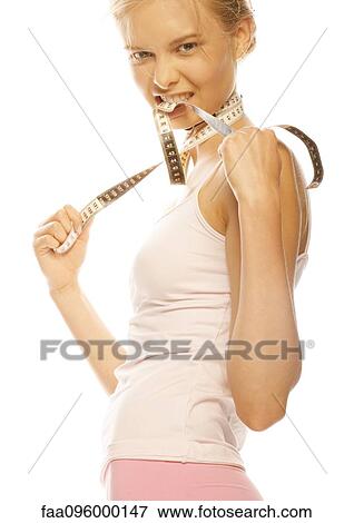 Stock Photo - Young woman standing with measuring tape around neck and between teeth. Fotosearch
