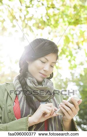 Stock Photo - Young woman using smartphone outdoors. Fotosearch
