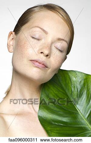 Stock Image - Young woman with tropical plant leaf, portrait. Fotosearch