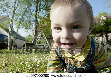 Stock Image - Baby crawling in grass, smiling cheerfully, portrait. Fotosearch