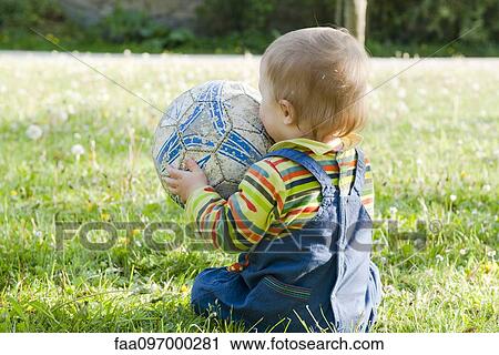 Baby sitting on grass playing with soccer ball, rear view View Large Photo Image Stock Image - Baby sitting on grass playing with soccer ball, rear view. Fotosearch