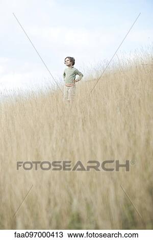 Stock Image - Boy standing in tall grass, looking away in thought. Fotosearch