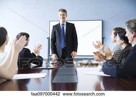 Stock Image - Business associates applauding colleague at meeting. Fotosearch